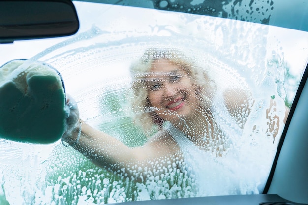 Una donna adulta lava il parabrezza di un'auto vista dall'interno dell'auto