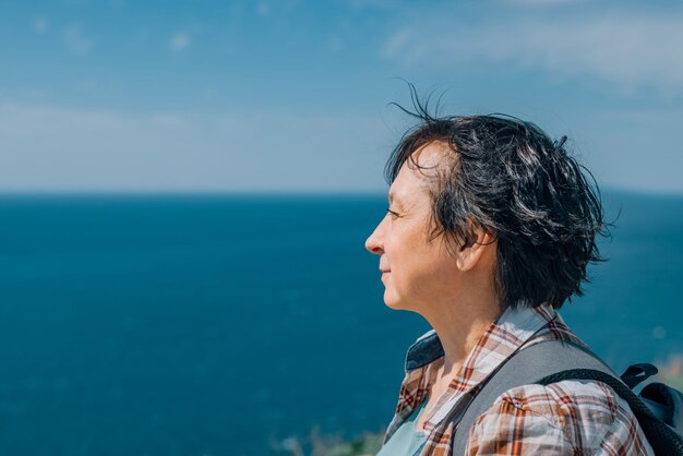 adult woman with a backpack went hiking in the mountains near the sea in summer sunny day for health