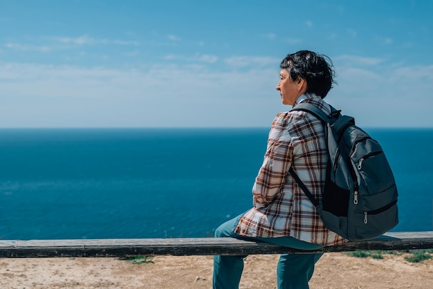 adult woman with a backpack went hiking in the mountains near the sea in summer sunny day for health