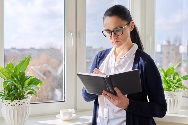 Adult woman with notepad and pencil at home near the window