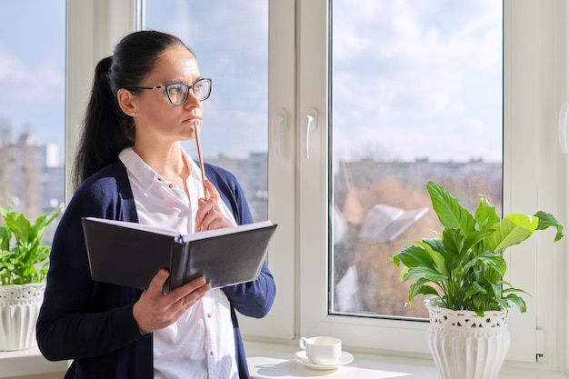 Adult woman with notepad and pencil at home near the window