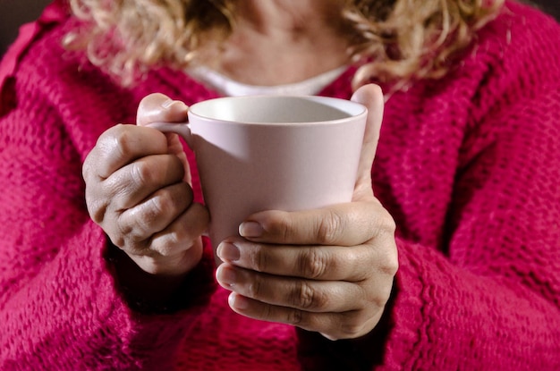 ラテコーヒーのカップを保持している赤いセーターと大人の女性