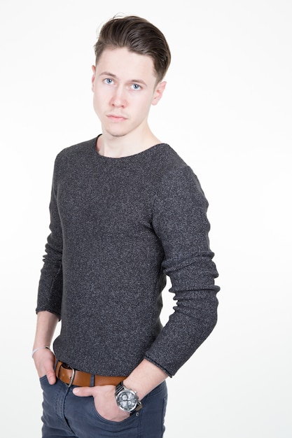 Adult young pleasant guy standing half turned with hands in jeans against gray background