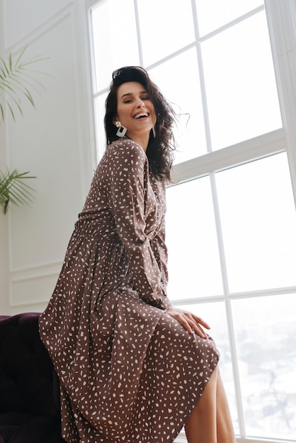 adult young woman is resting in a beautiful feminine dress in a bright room by the window