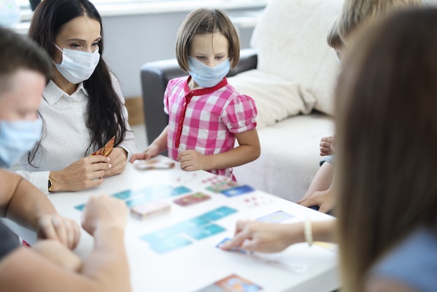 Adults and children in medical protective masks play board games