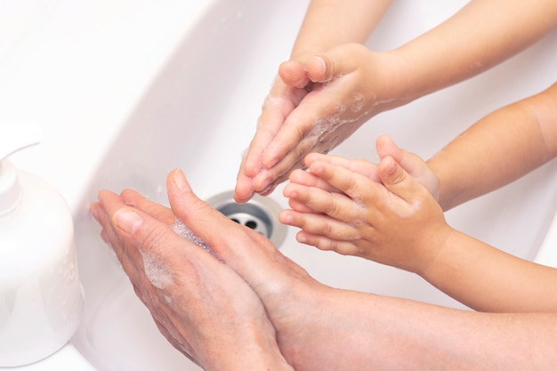 大人も子供も手を洗います。抗菌石鹸の泡で手。細菌、コロナウイルスに対する保護。手指衛生。水で手を洗う。