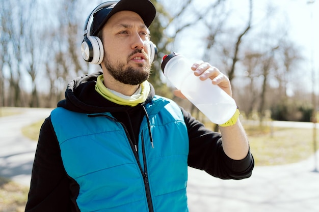 ノースリーブのスウェットシャツに野球帽をかぶったワイヤレスヘッドホンを身に着けている上級ランナー