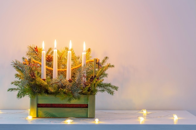 Advent decoration with fir branches and four burning candles in wooden basket on white background