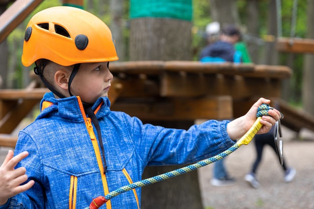 Adventure climbing high wire park - little boy on course in mountain helmet and safety equipment.