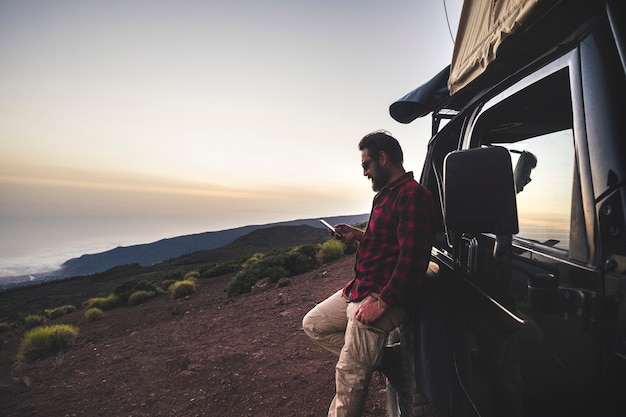 L'uomo viaggiatore esploratore di avventura usa il telefono cellulare con connessione internet in un luogo selvaggio di montagna durante l'escursione di viaggio con auto fuoristrada nera e tenda sul tetto - concetto di persone libere