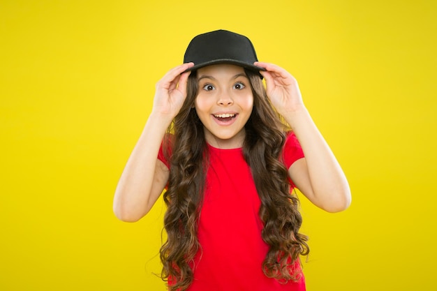 Adventure of Fashion. happy childhood. beauty and fashion. small girl with long hair. cool girl with long curly hair. kid fashion. happy girl in trendy hipster cap. hipster child on yellow background.