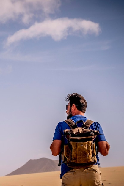 Adventure lifestyle with explorer man with backpack viewed from back walking in the desert and mountains alone wild people alternative travel vacation alone in outdoor wild nature