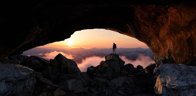 Foto uomo d'avventura in piedi in una grotta rocciosa paesaggio di montagna coperto di neve sullo sfondo