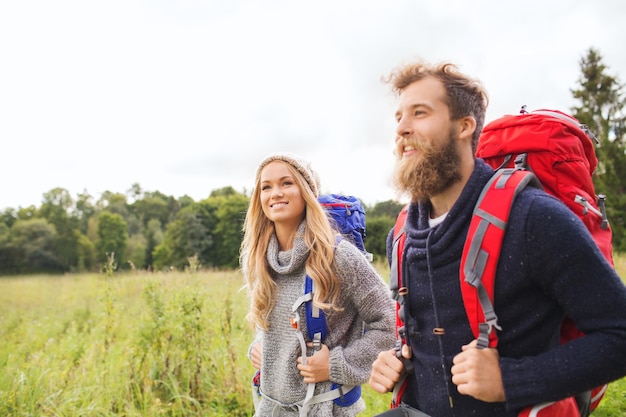 Фото Приключения, путешествия, туризм, походы и концепция людей - улыбающаяся пара, гуляющая с рюкзаками на открытом воздухе