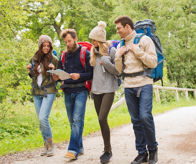 adventure, travel, tourism, hike and people concept - group of smiling friends walking with backpacks and map walking outdoors