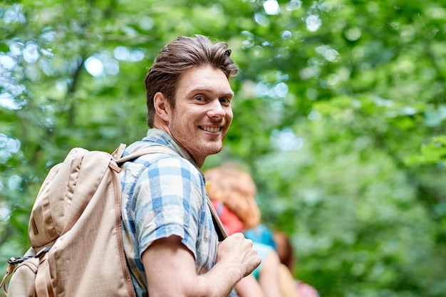 приключения, путешествия, туризм, походы и концепция людей - группа улыбающихся друзей, идущих с рюкзаками в лесу