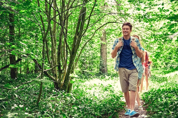 adventure, travel, tourism, hike and people concept - group of smiling friends walking with backpacks in woods