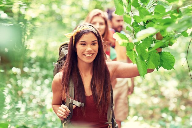 Adventure, travel, tourism, hike and people concept - group of smiling friends walking with backpacks in woods