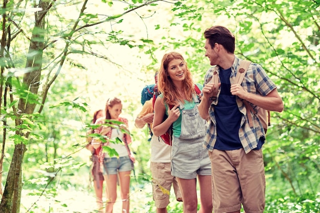 Photo adventure, travel, tourism, hike and people concept - group of smiling friends walking with backpacks in woods