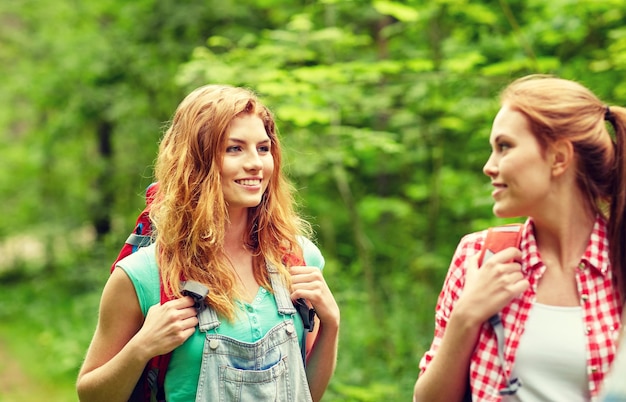 adventure, travel, tourism, hike and people concept - group of smiling friends walking with backpacks in woods