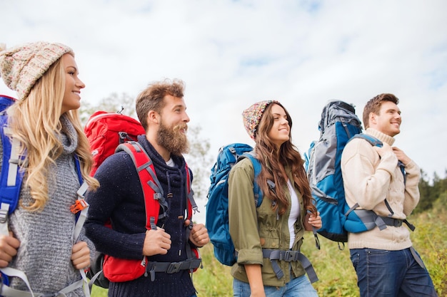 adventure, travel, tourism, hike and people concept - group of smiling friends walking with backpacks