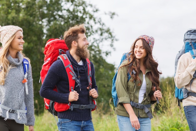 adventure, travel, tourism, hike and people concept - group of smiling friends walking with backpacks