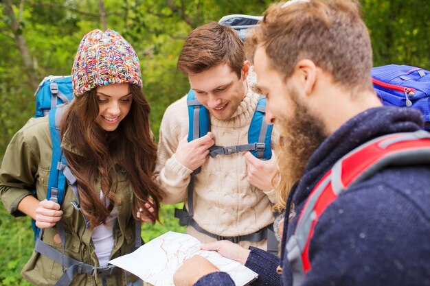 Concetto di avventura, viaggio, turismo, escursione e persone - gruppo di amici sorridenti con zaini e mappa all'aperto