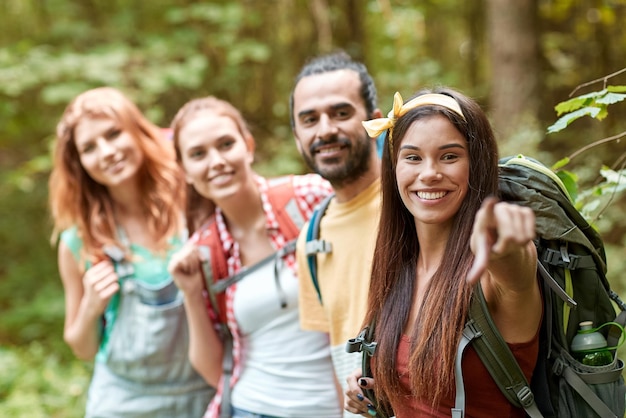 adventure, travel, tourism, hike and people concept - group of smiling friends with backpacks pointing finger in woods