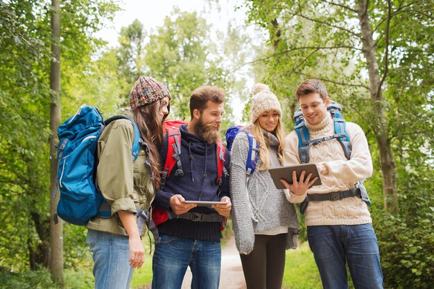 adventure, travel, tourism, hike and people concept - group of smiling friends with backpacks and tablet pc computers outdoors