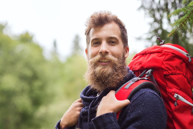 adventure, travel, tourism, hike and people concept - smiling man with beard and red backpack hiking