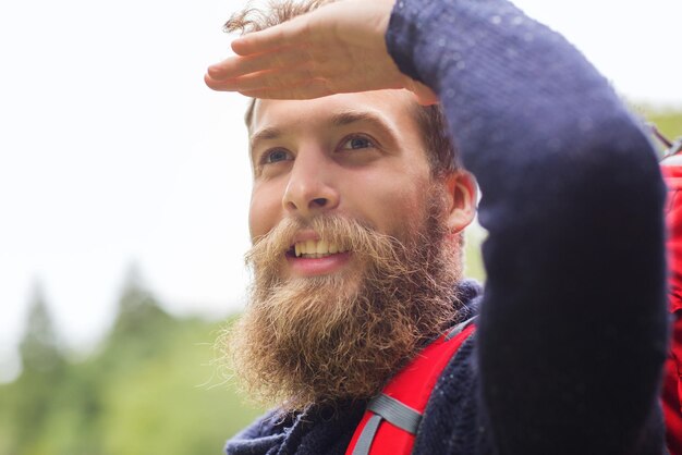 Concetto di avventura, viaggi, turismo, escursione e persone - uomo sorridente con barba e zaino rosso escursionismo