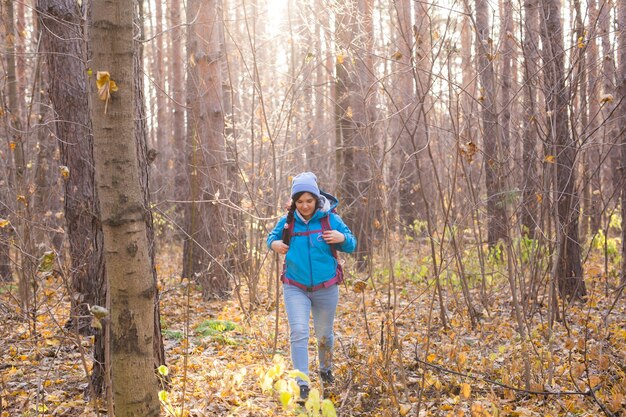 Photo adventure, travel, tourism, hike and people concept - smiling tourist woman walking with backpacks over autumn natural forest.