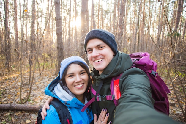 Adventure, travel, tourism, hike and people concept - tourists smiling couple taking selfie over trees.