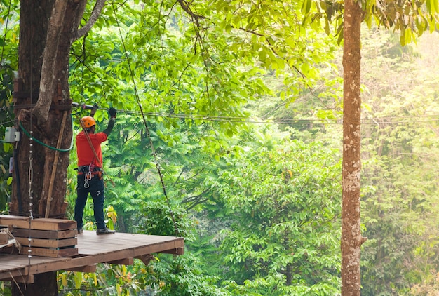 Adventure zipline high wire park - persone in rotta nel casco da montagna e attrezzatura di sicurezza, pronte a scendere su zipline nella foresta, sport estremi