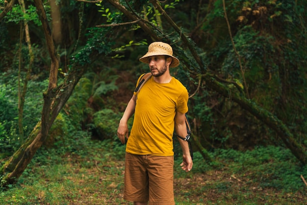 사진 노란색 티셔츠를 입은 모험적인 백인 남자가 숲에서 배낭을 메고 있다
