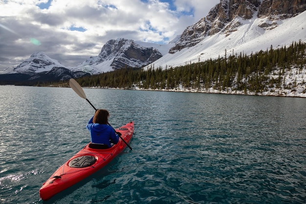 Авантюрная девушка на каяке в ледниковом озере, окруженном канадскими Скалистыми горами