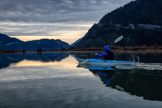 Adventurous man kayaking in peaceful water during a cloudy winter sunset