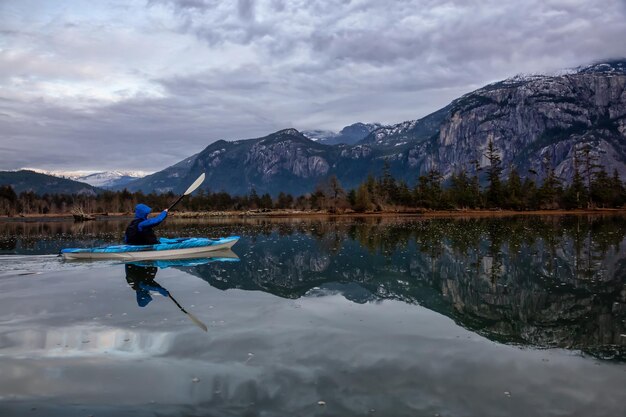 Uomo avventuroso in kayak in acque tranquille durante un nuvoloso tramonto invernale