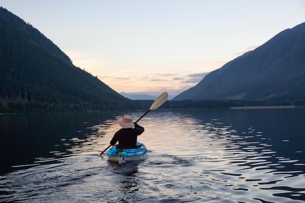 カナダの山の風景のそばで水中でカヤックをする冒険的な男