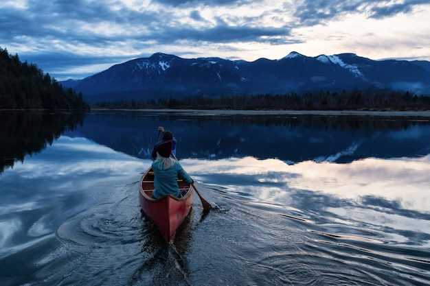 Adventurous people on a wooden canoe are enjoying the Canadian Mountain Landscape