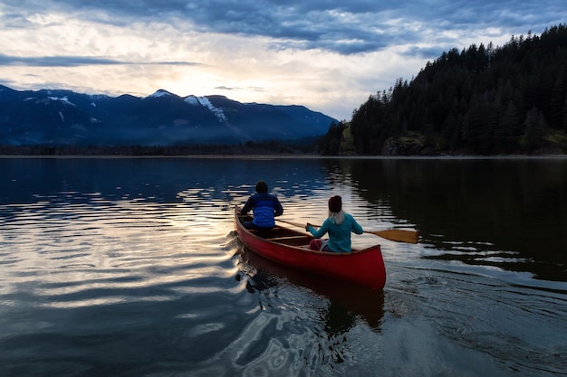 Adventurous people on a wooden canoe are enjoying the Canadian Mountain Landscape