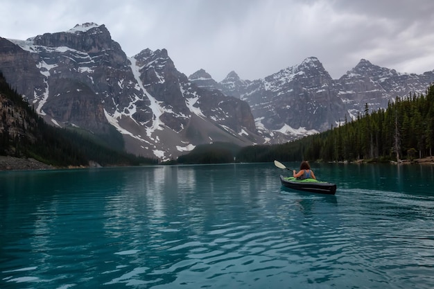 Adventurous woman kayaking in Moraine Lake during a striking cloudy sunset