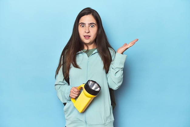 Adventurous woman with backpack on blue surprised and shocked