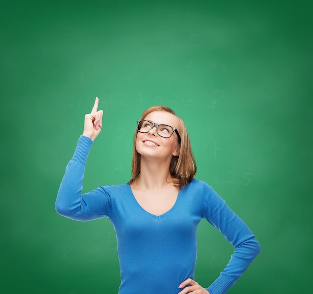 advertisement concept - attractive young woman in casual clothes and black eyeglasses pointing her finger up