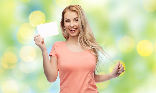 Photo advertisement, invitation, message and people concept - smiling young woman or teenage girl with blank white paper card over summer green lights background