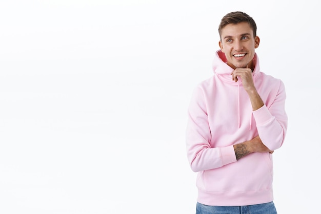 Advertisement people and lifestyle concept Portrait of handsome blond guy in pink hoodie smiling as looking left at empty space for company banner promo checkout good deal