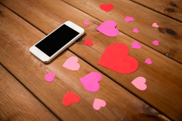 advertisement, romance, valentines day and holidays concept - close up of smartphone and hearts on wood