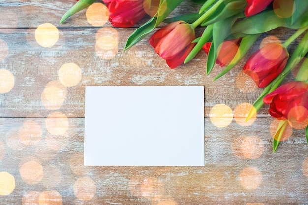 advertisement, valentines day, greeting and holidays concept - close up of red tulips and blank paper or letter on wooden background over lights