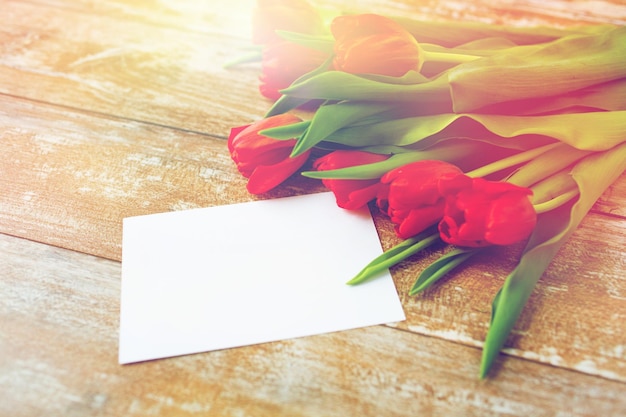 advertisement, valentines day, greeting and holidays concept - close up of red tulips and blank paper or letter on wooden background