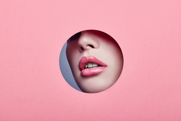 Advertising Beautiful plump lips bright pink color, woman looks in hole